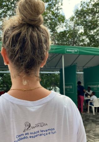 Voluntária de costas com a camiseta da missão: “Com as mãos levamos cuidado, esperança e luz.”